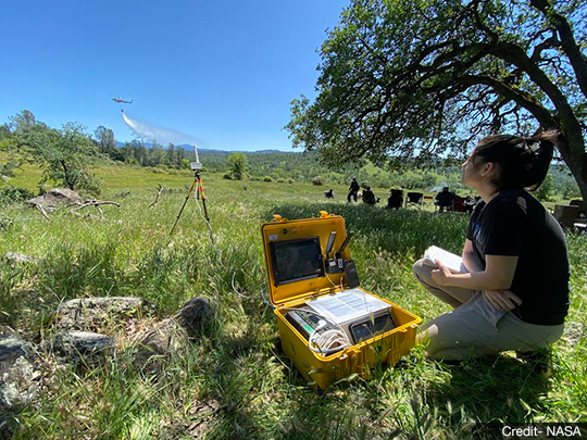 Yasmin Arbab, a research associate at NASA's Ames Research Center, tests a prototype device designed for firefighting drone operators, while piloted aircraft perform fire-training operations in the sky, in Redding, California, on May 3, 2022. Intended to help scale up the use of unmanned aircraft systems (UAS) - or drones - in disaster response, the UAS pilot's kit shown here was developed by NASA's Scalable Traffic Management for Emergency Response Operations (STEReO) project